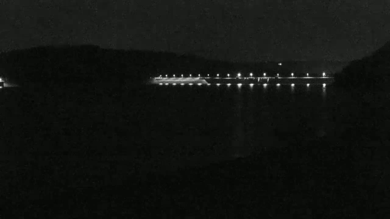 A long, illuminated dam is visible at night, extending across a dark body of water.