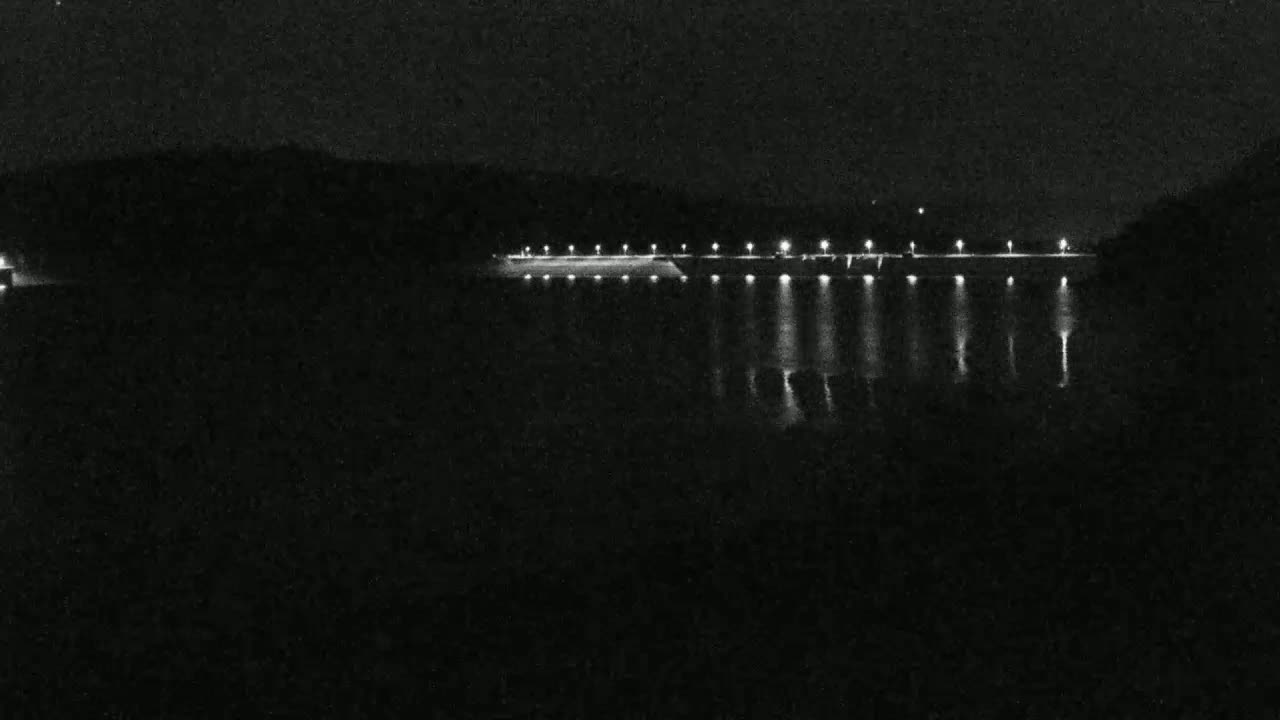A long, illuminated dam is visible at night, reflecting light onto dark water.