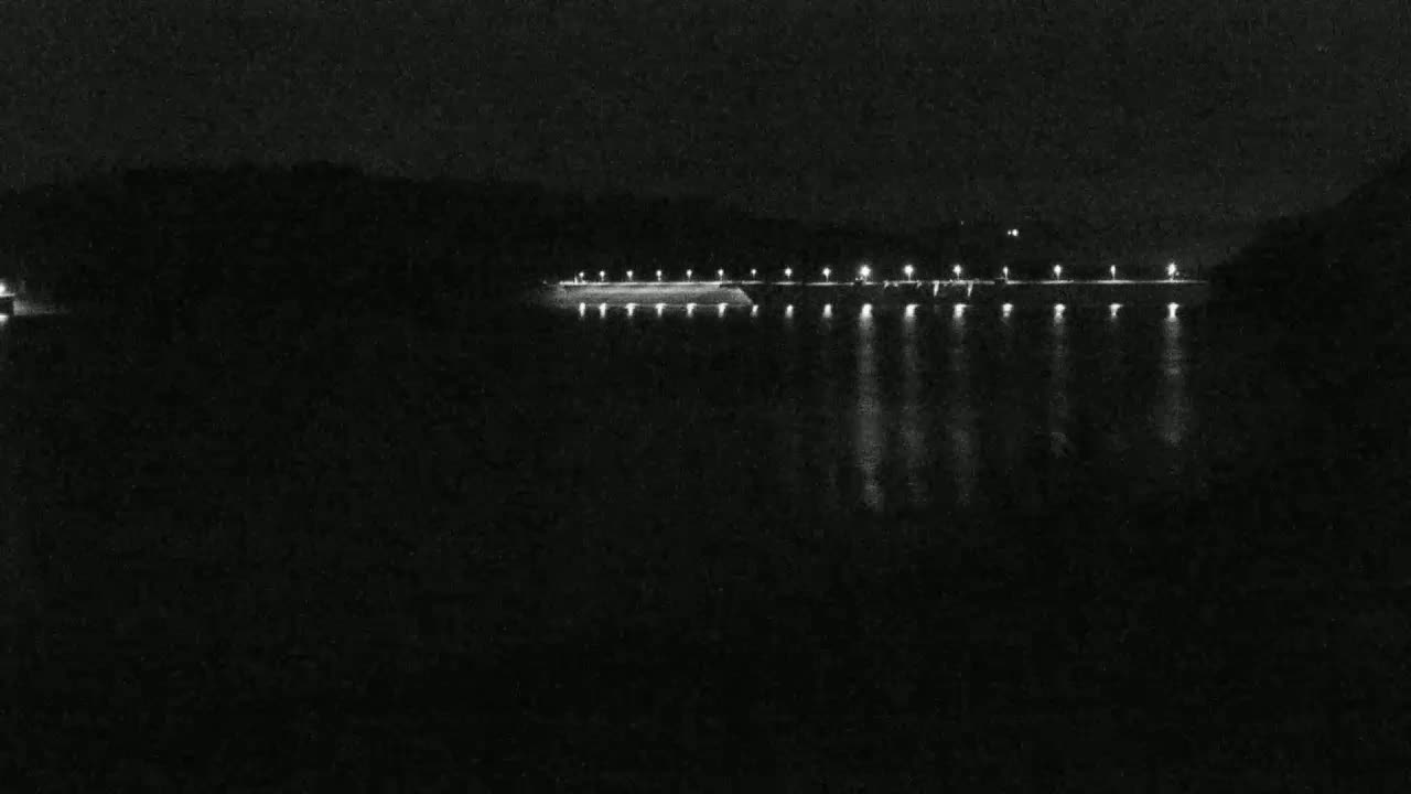 A long, illuminated structure stretches across a dark body of water at night.