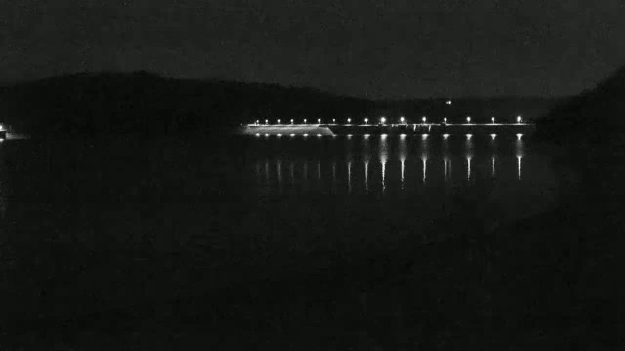 A long, illuminated dam stretches across a dark, still body of water at night.