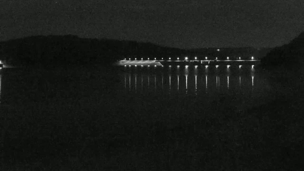 A lighted dam is reflected in a dark body of water at night.