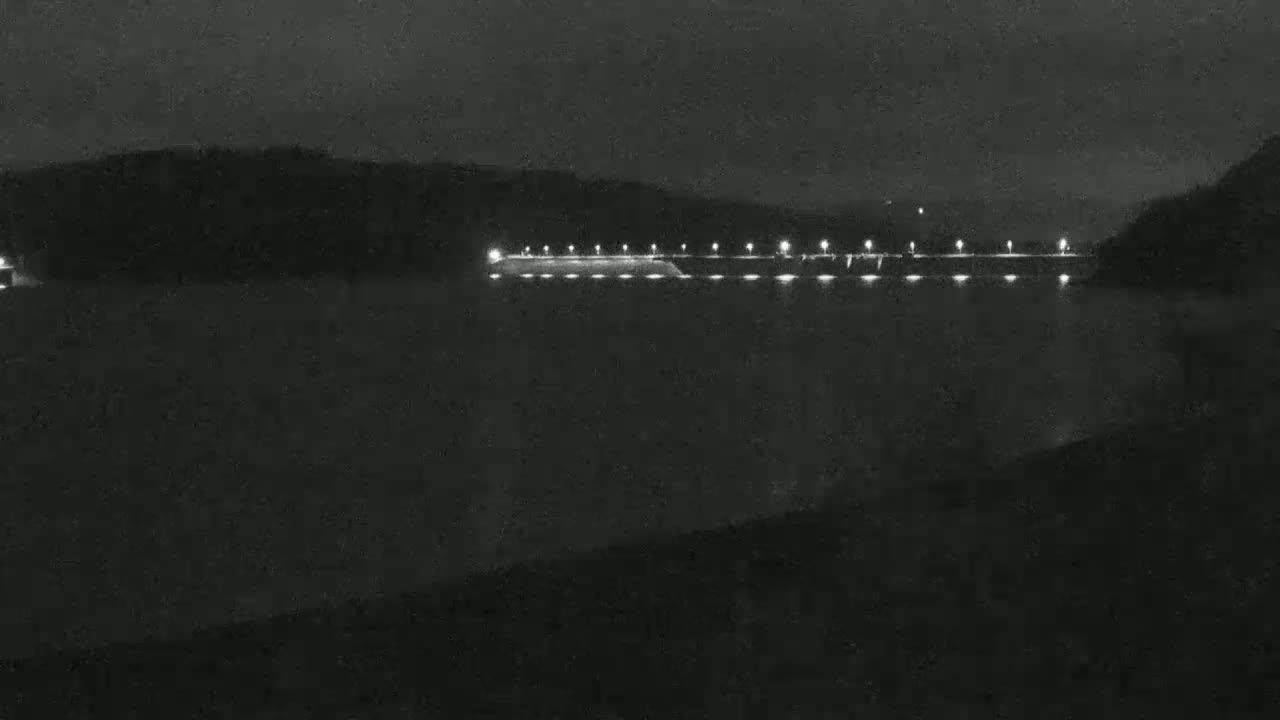 A long, illuminated dam stretches across a dark body of water under a nighttime sky.