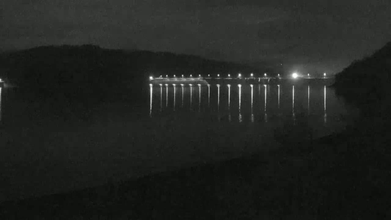 A long, illuminated structure stretches across a dark body of water at night.