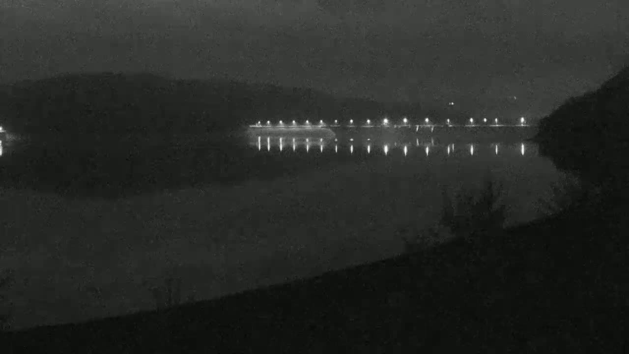A nighttime view of a calm body of water reflecting the lights of a distant structure on a dark, foggy night.