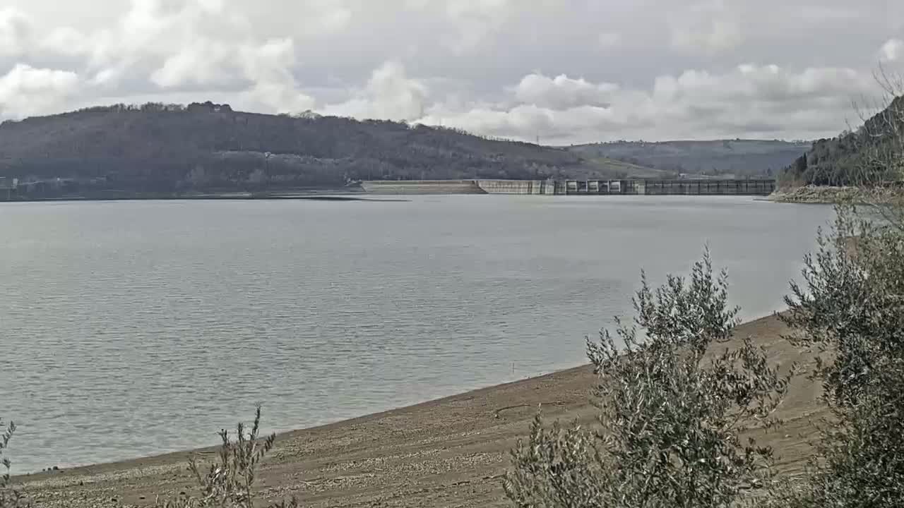 A large body of water, low on water level, is seen behind a dam on an overcast day.