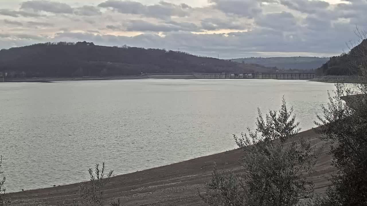 A calm lake stretches out under a cloudy sky, backed by a line of dark hills.