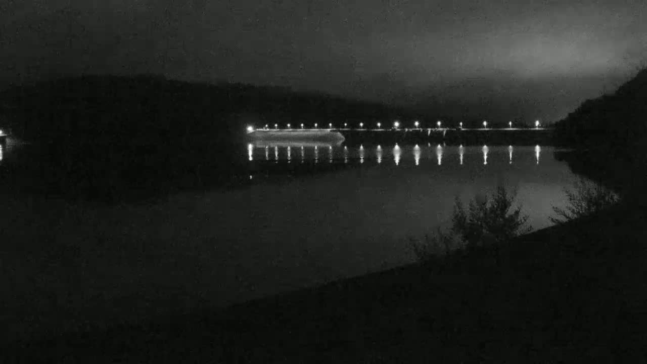 A nighttime view of a calm body of water reflecting the lights of a dam.