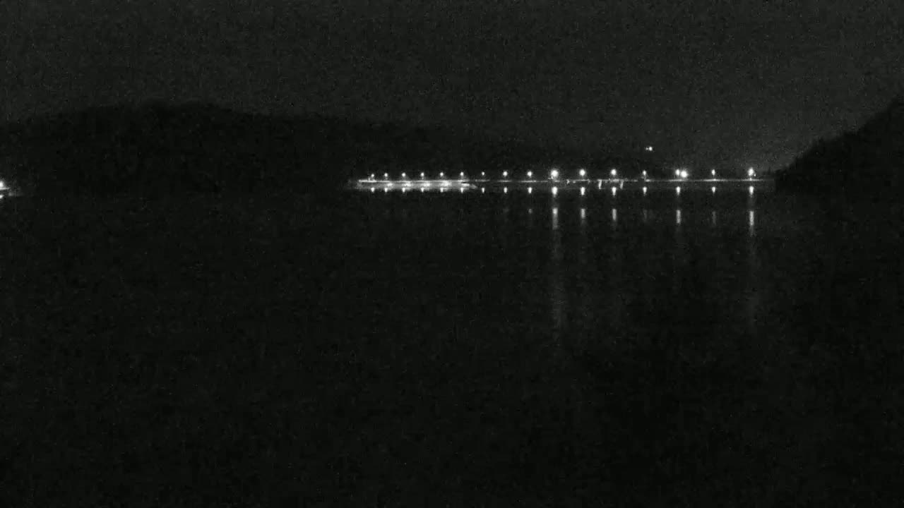 A dark body of water reflects the lights of a distant shoreline at night.