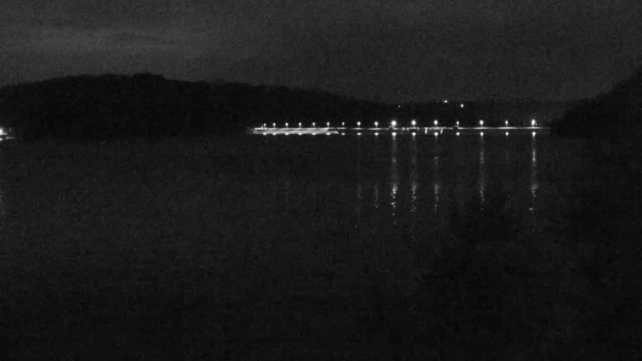 At night, a body of dark water reflects the lights of a distant shoreline.