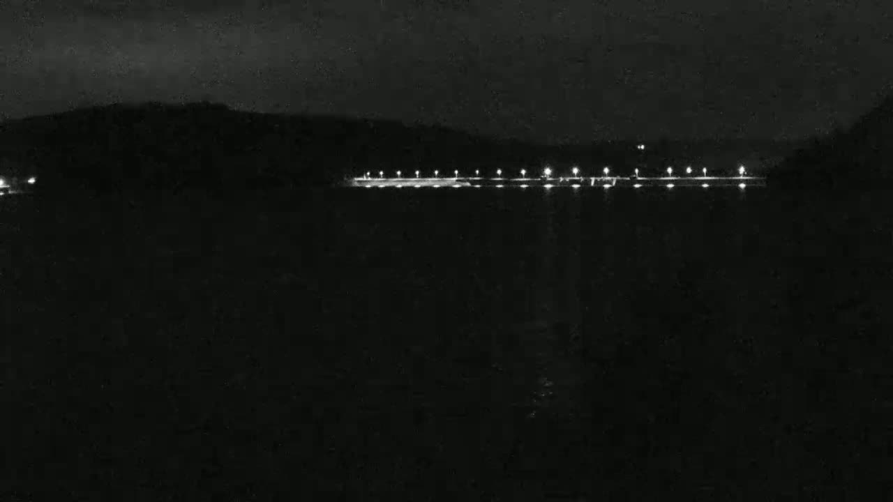 A nighttime view of a body of water with a line of lights across the far shore under a dark, cloudy sky.