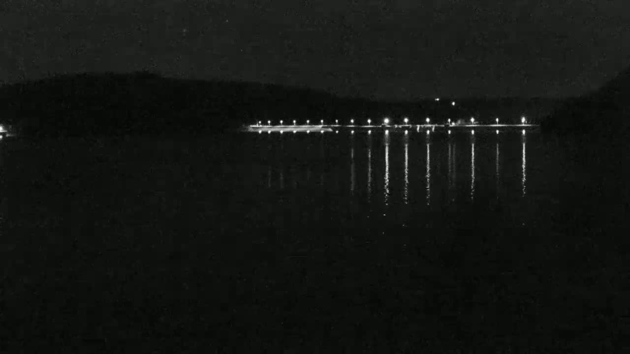 At night, a dark body of water reflects the lights of a shoreline structure.