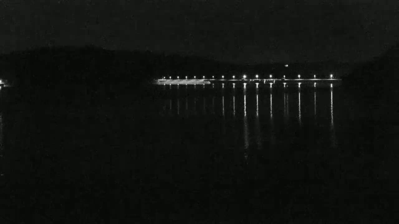 A dark body of water reflects the lights of a long, low structure at night.