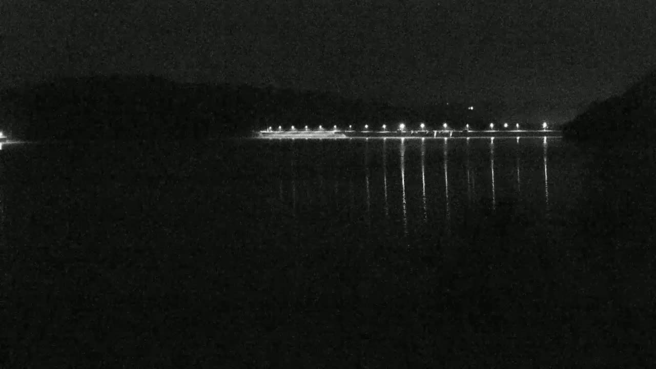 A nighttime view of a calm body of water reflecting the lights of a distant shoreline.
