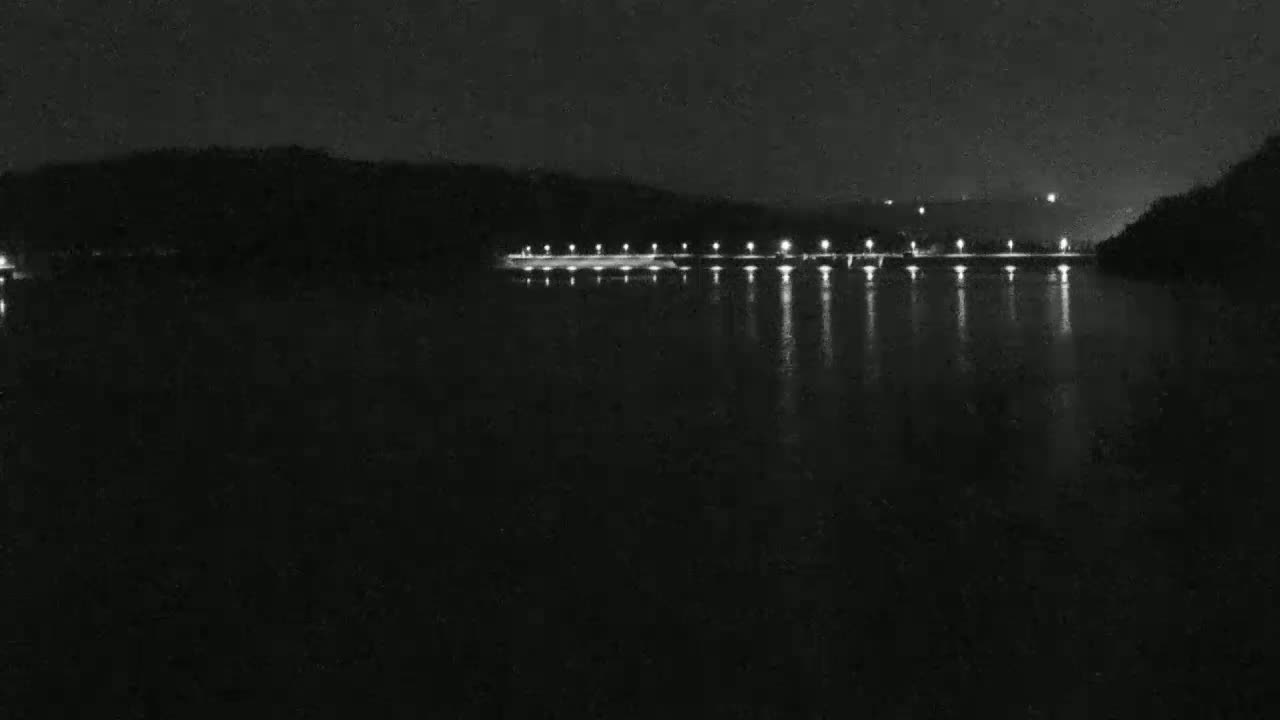 Lights illuminate a dark body of water at night, reflecting off the still surface, with a dark landmass visible in the background.