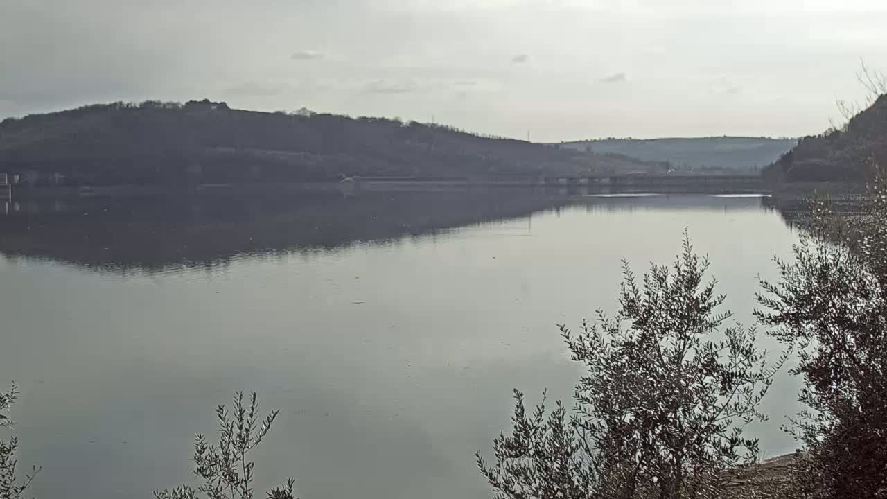 A calm lake reflects a hazy sky and distant hills under overcast conditions.