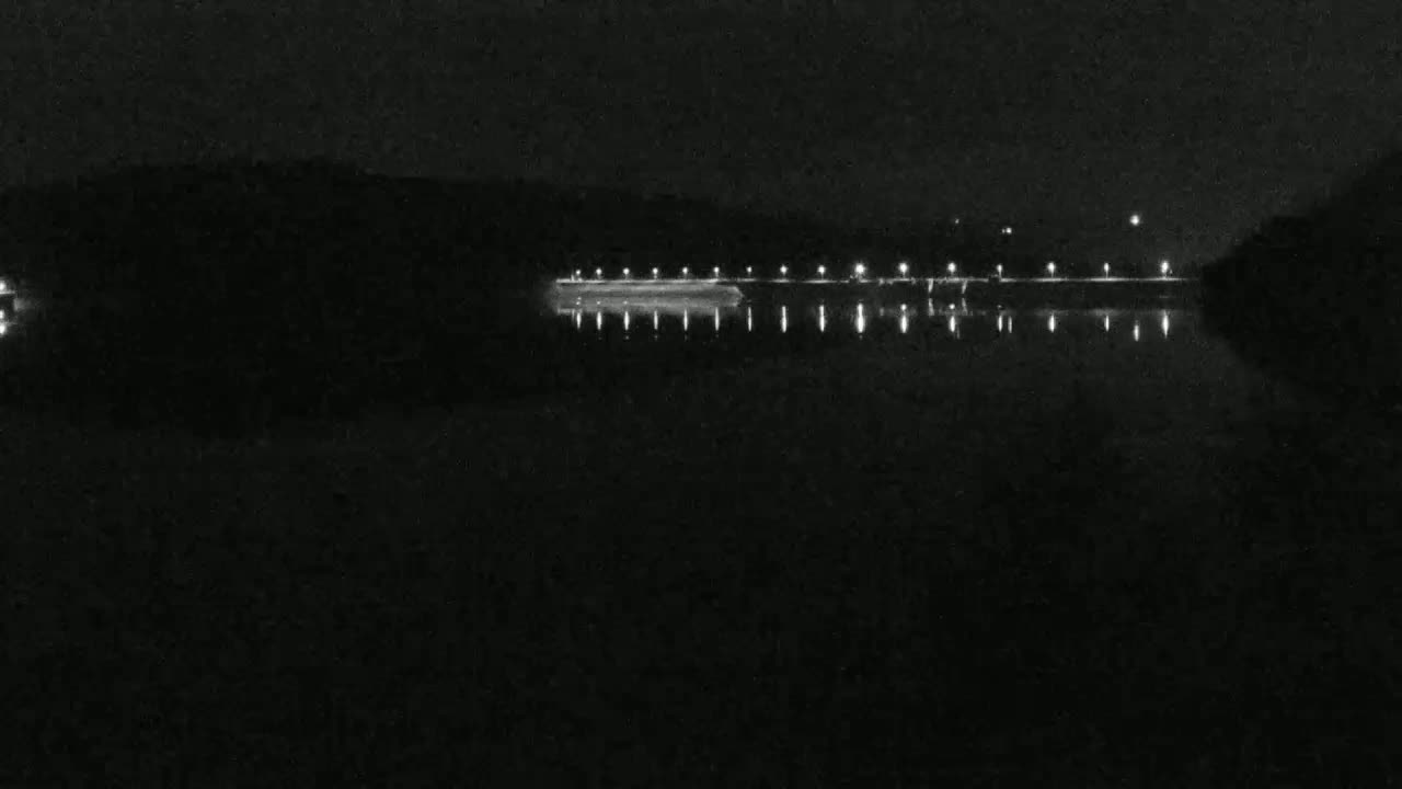 A dark body of water reflects the lights of a distant shoreline at night.