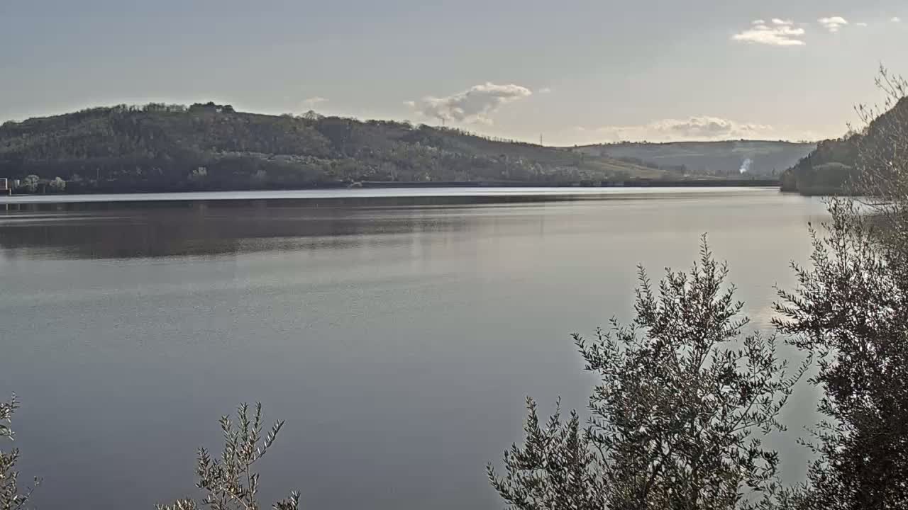A calm lake reflecting a mostly clear sky is surrounded by hills covered in low-lying vegetation.