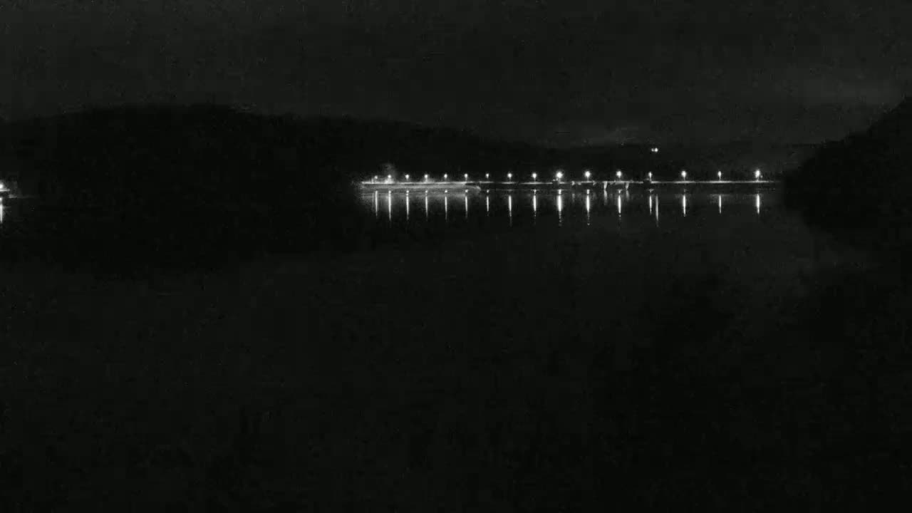 At night, a calm body of water reflects the lights of a distant shoreline.