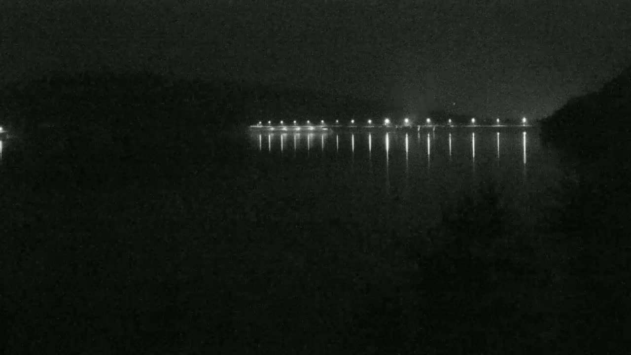 A dark body of water reflects the lights of a distant shoreline at night.