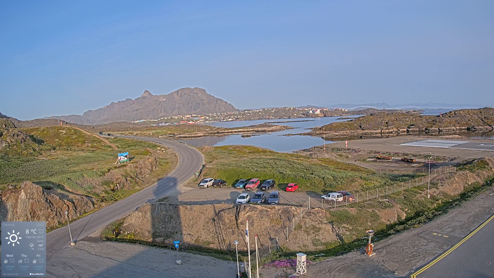 A mostly cloudy day reveals a rocky, coastal landscape with calm water, a small airfield, and a tall communication tower.