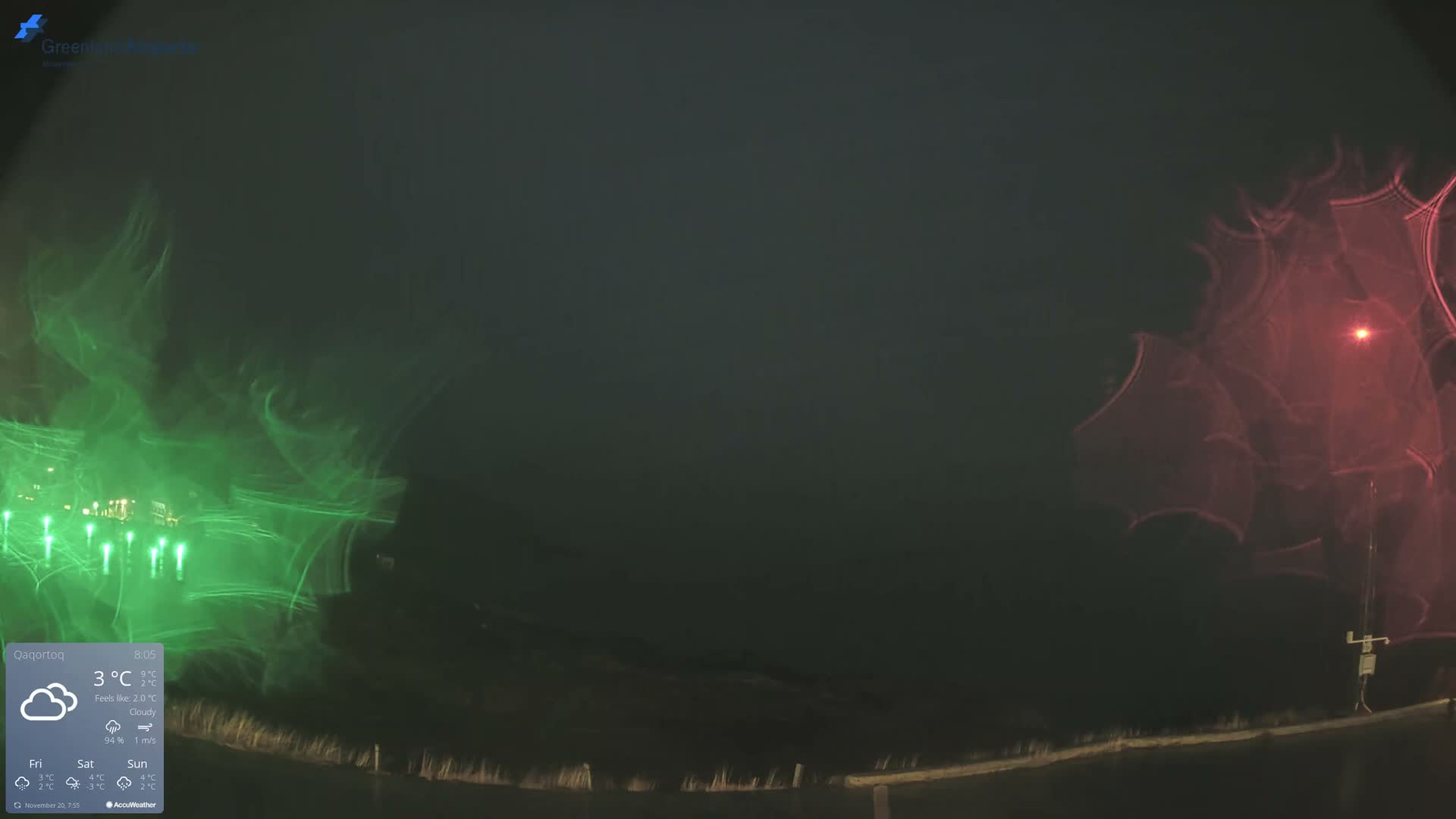 The image displays a dark, cloudy night scene featuring prominent green light flares on the left, a distinct red light with an expansive lens flare on the right, and a dimly visible, undulating ground in the foreground.