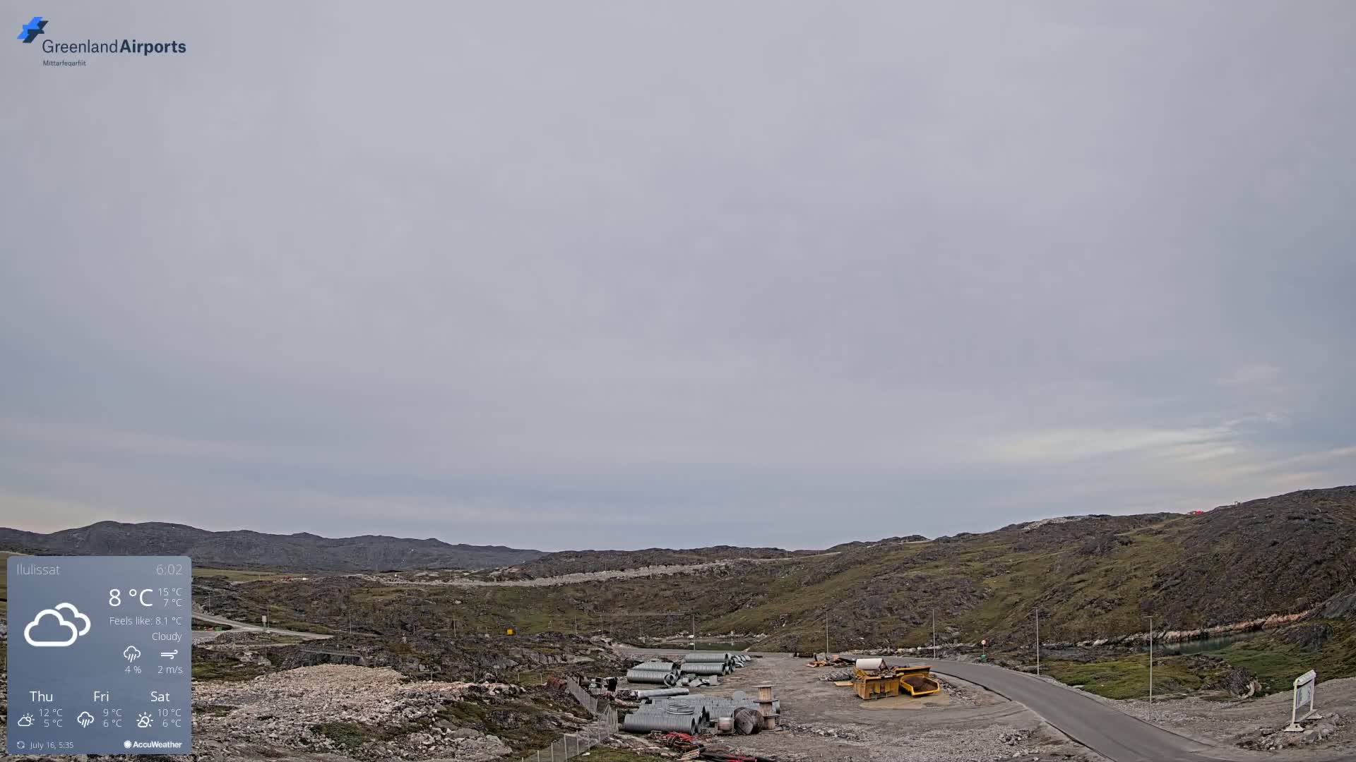 A cloudy, overcast day reveals a rocky, sparsely vegetated landscape with construction materials and machinery near a paved road.