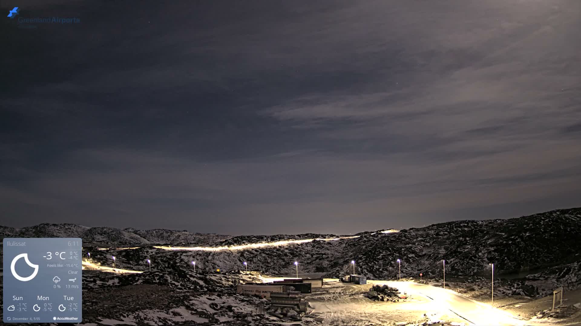 A winding, brightly lit road traverses a snow-dusted, rocky landscape at night beneath a mostly clear sky with subtle cloud patterns.