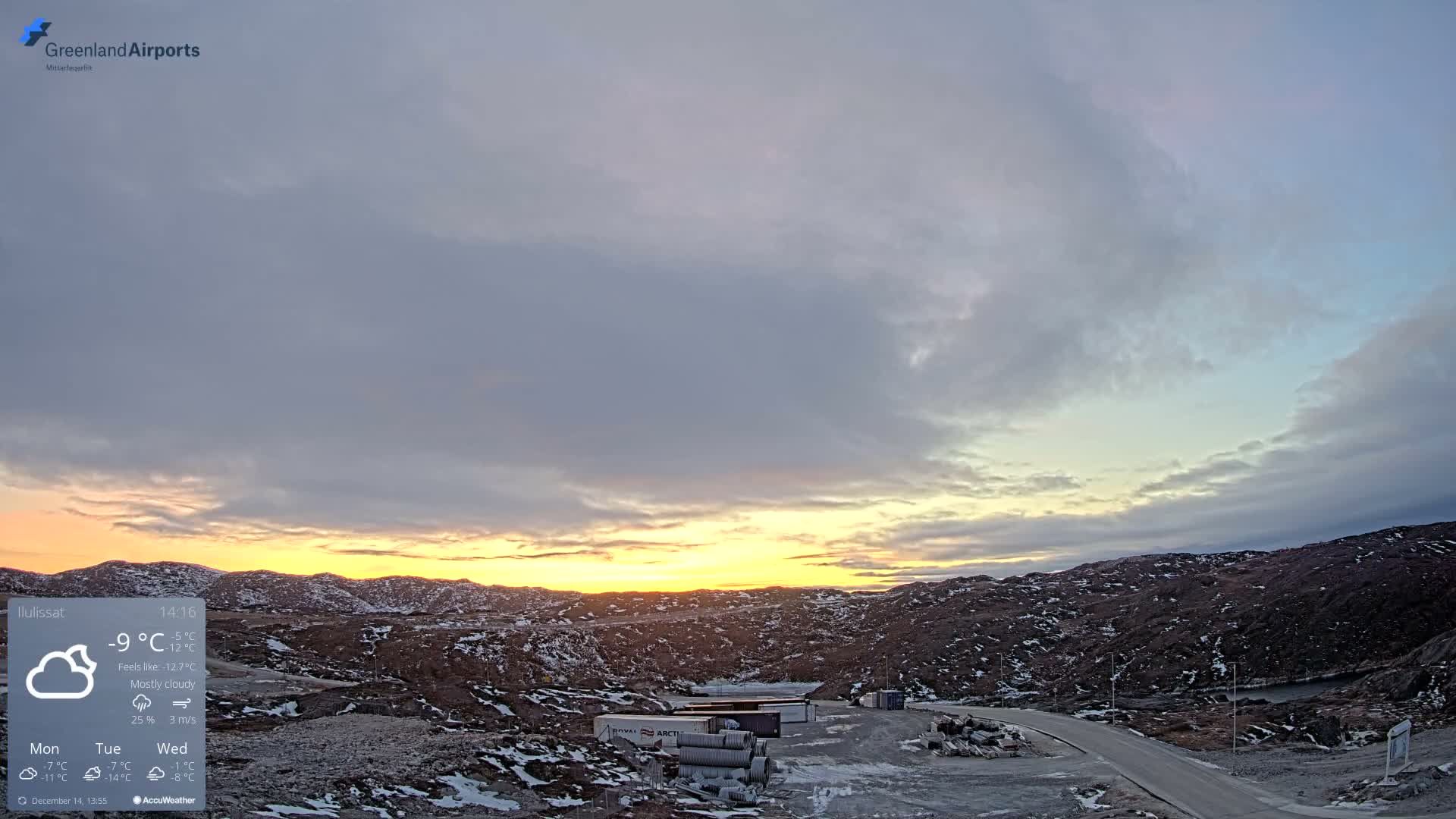 A winding, brightly lit road traverses a snow-dusted, rocky landscape at night beneath a mostly clear sky with subtle cloud patterns.