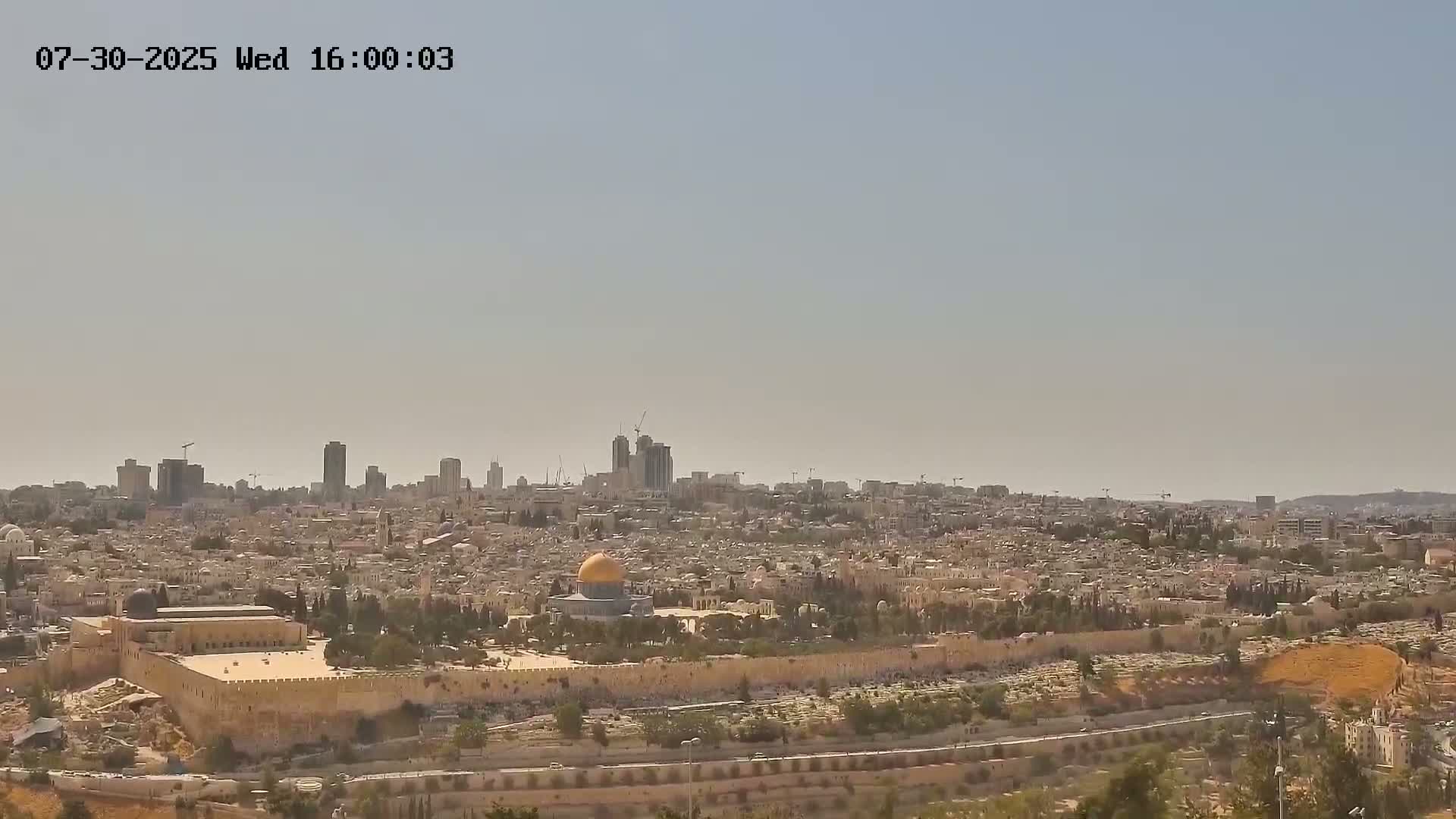 A sprawling city with a gold-domed building at its center is visible under a clear blue sky.