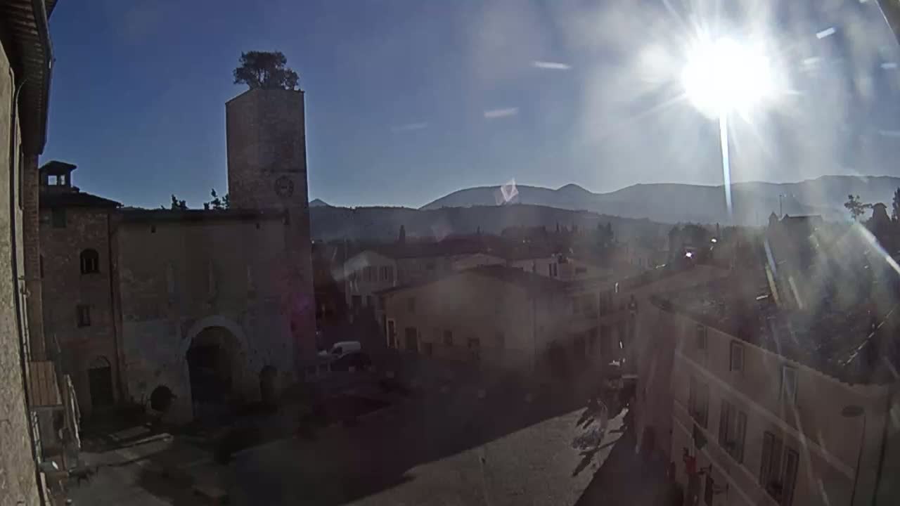A sunny day reveals a stone town square with buildings, a tall tower, and distant mountains.