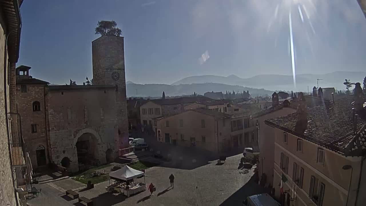 A sunny day reveals a town square with stone buildings, a clock tower topped with a tree, and distant hazy mountains.