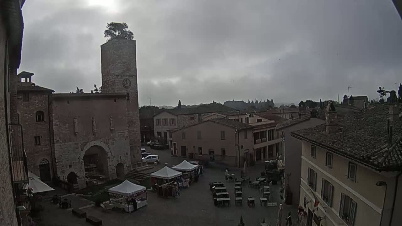 A town square with several buildings, market stalls, and outdoor seating under an overcast sky.
