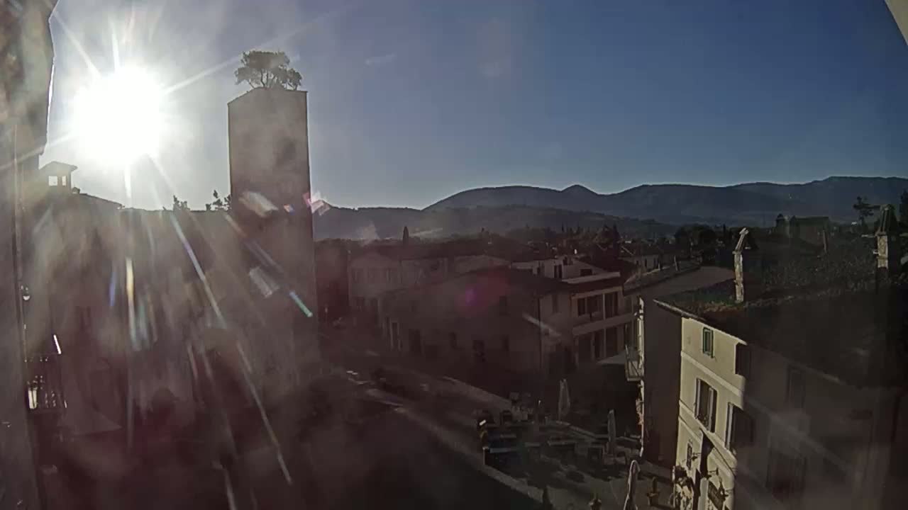 A sun-drenched view of a town nestled in a valley, with mountains in the distance under a clear sky.