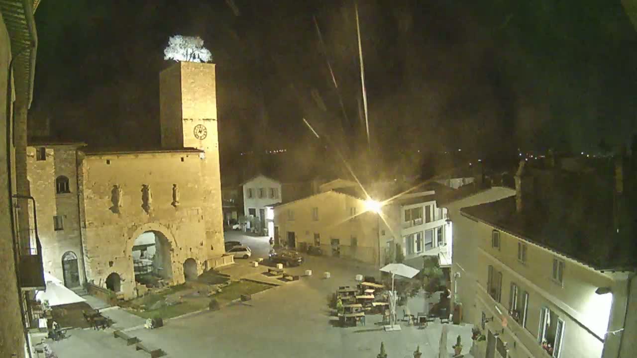 A nighttime view of a town square with a stone building and clock tower, under a slightly hazy sky.