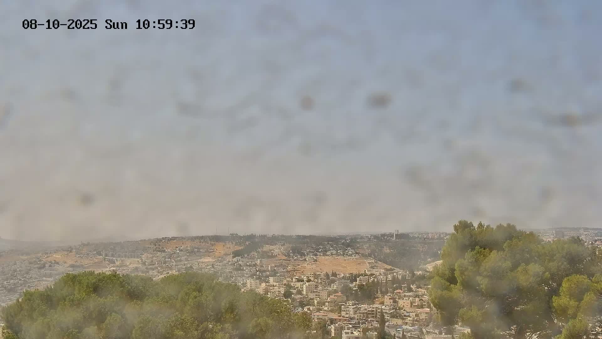 A hazy view shows a sprawling city nestled in hills, partially obscured by a dusty or smoky atmosphere.