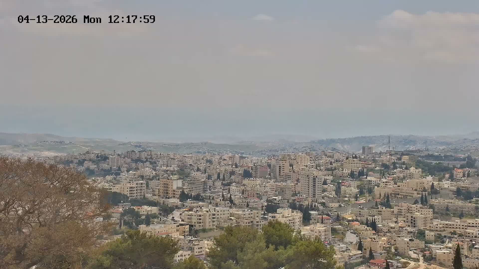 A panoramic view reveals a sprawling city nestled among hazy hills under a partly cloudy sky.