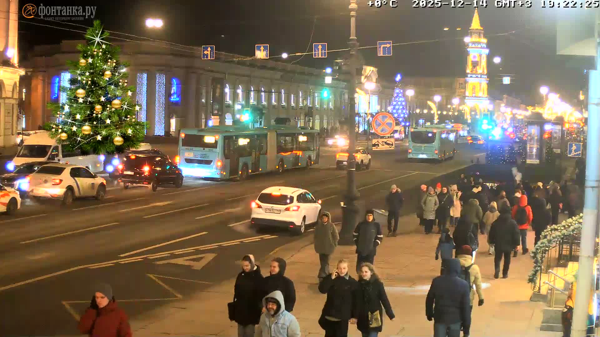 An overcast daytime city scene features a large decorated Christmas tree next to a busy road with numerous cars, a prominent sidewalk filled with pedestrians, and classical buildings with a distant clock tower under a grey sky.