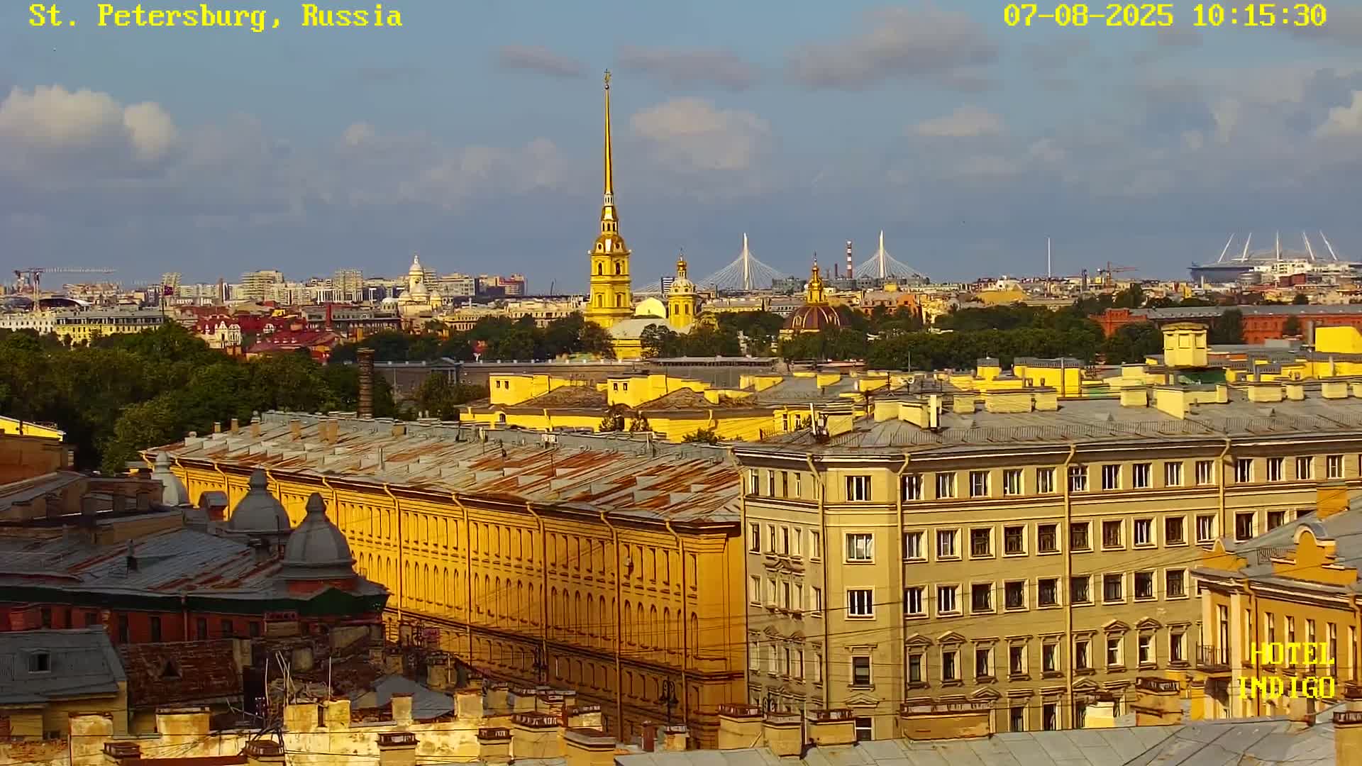 A partly sunny cityscape view shows many yellow buildings, a tall spire, and bridges in the distance.