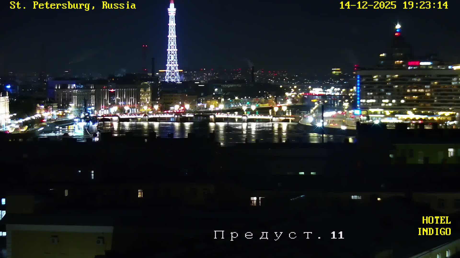 A foggy nighttime cityscape depicts illuminated buildings and streets, with numerous lights reflecting on a wide body of water where a large vessel is moored.