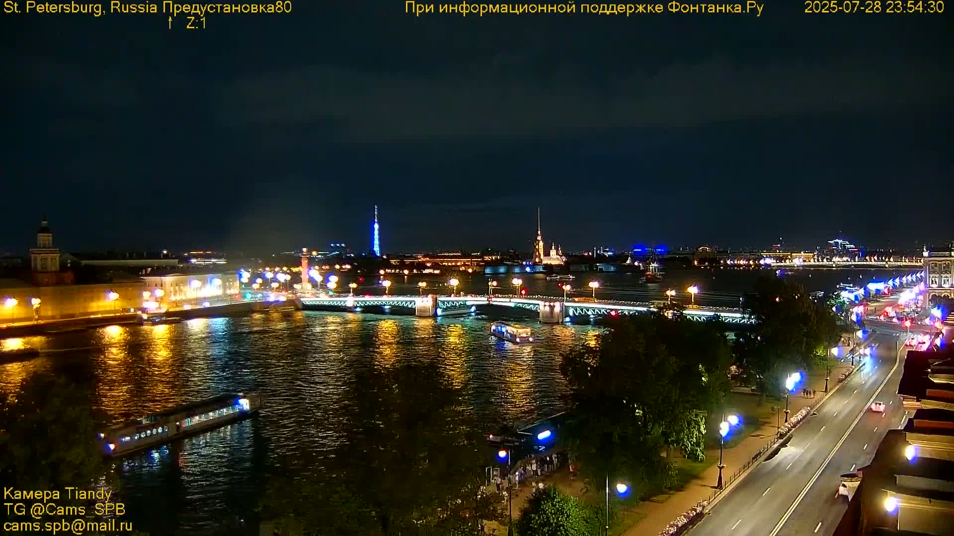 A nighttime view of a city illuminated with lights across a river and bridge, under a clear, dark sky.