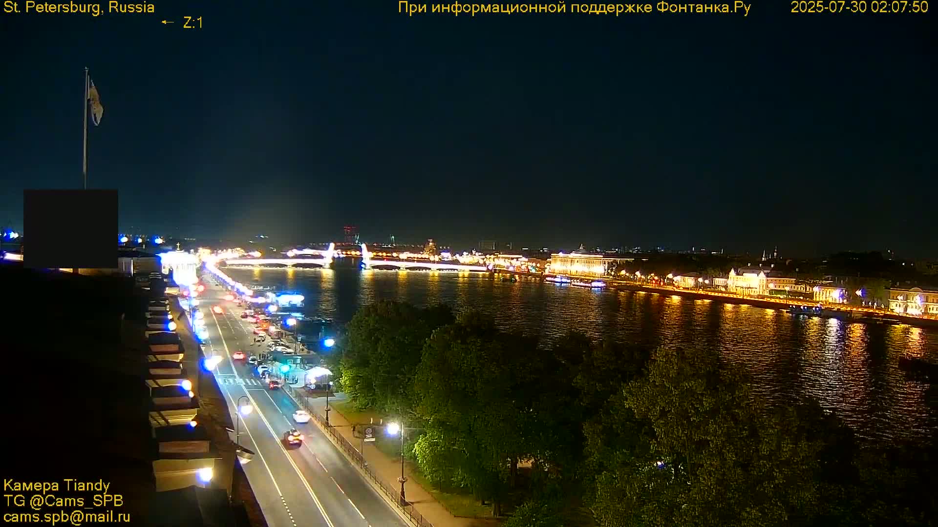A nighttime view of a city illuminated with lights across a river and bridge, under a clear, dark sky.