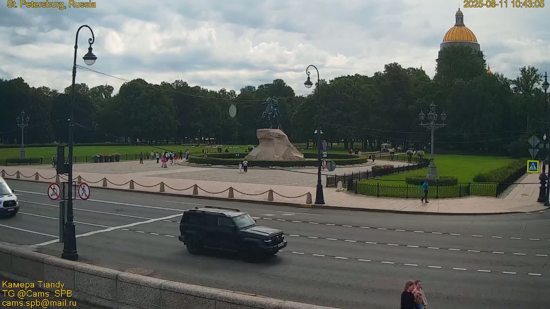 A partly cloudy day shows an equestrian statue in a park with a golden-domed building in the background,  viewed from across a street with cars and pedestrians.