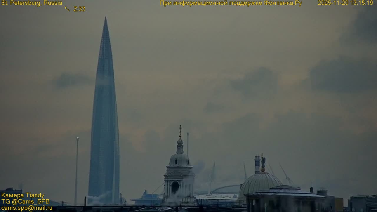 A towering, modern skyscraper looms over traditional domed buildings in an urban landscape, all beneath a gloomy, overcast sky with steam rising, indicating cold weather.