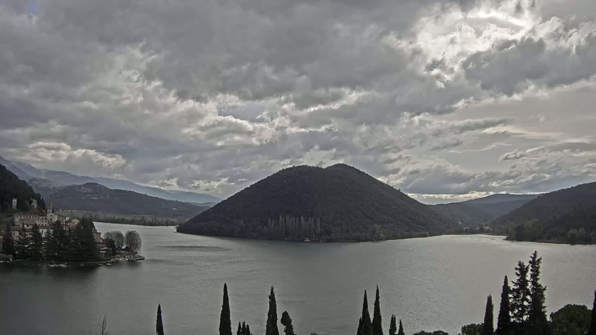 A lake surrounded by mountains and a small island with buildings under a cloudy sky.