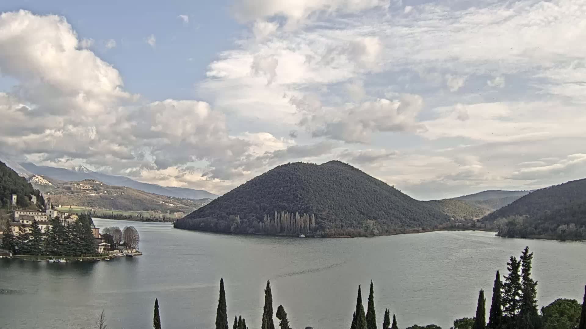 A lake is surrounded by mountains and trees under a partly cloudy sky.