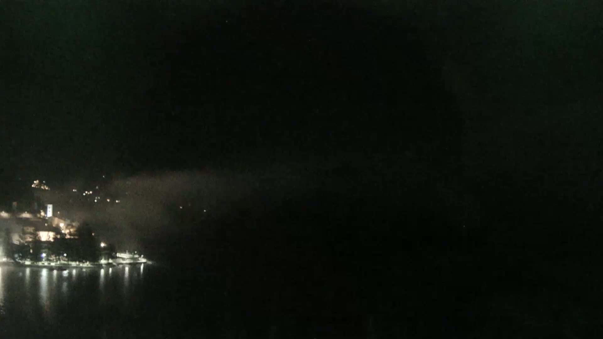 A nighttime, foggy view shows a town's lights across a dark body of water.