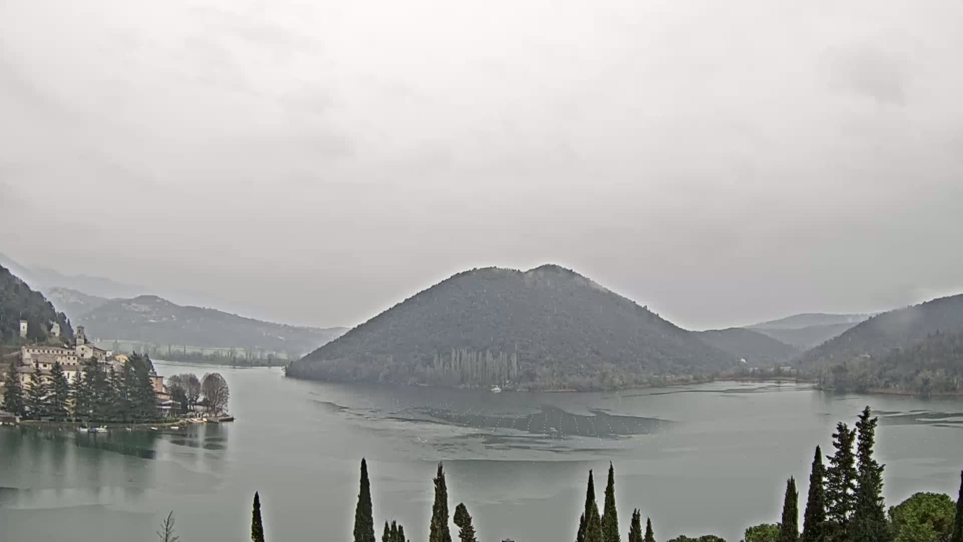 A lake is surrounded by hills and a small village under an overcast sky.