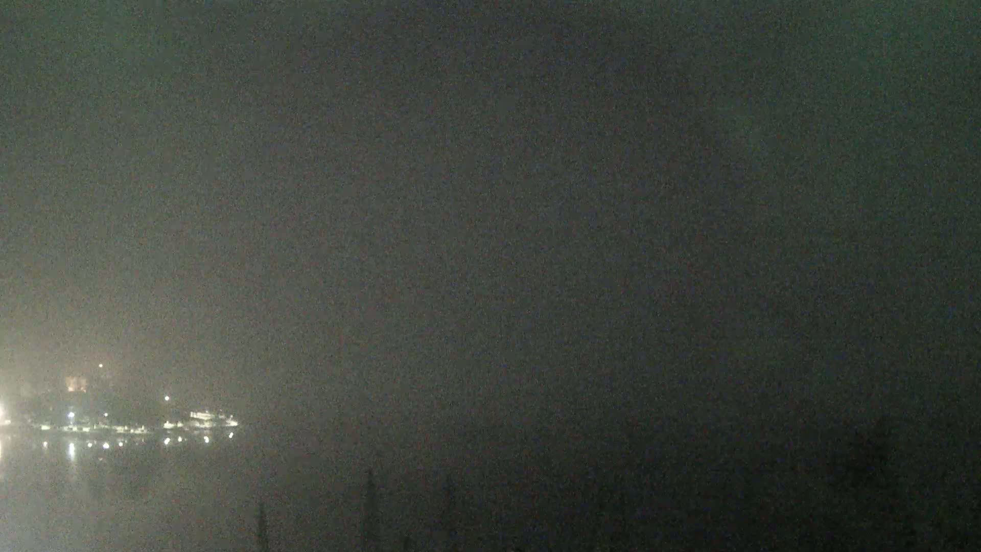 A hazy night scene shows a body of water reflecting dim lights from a distant shoreline.