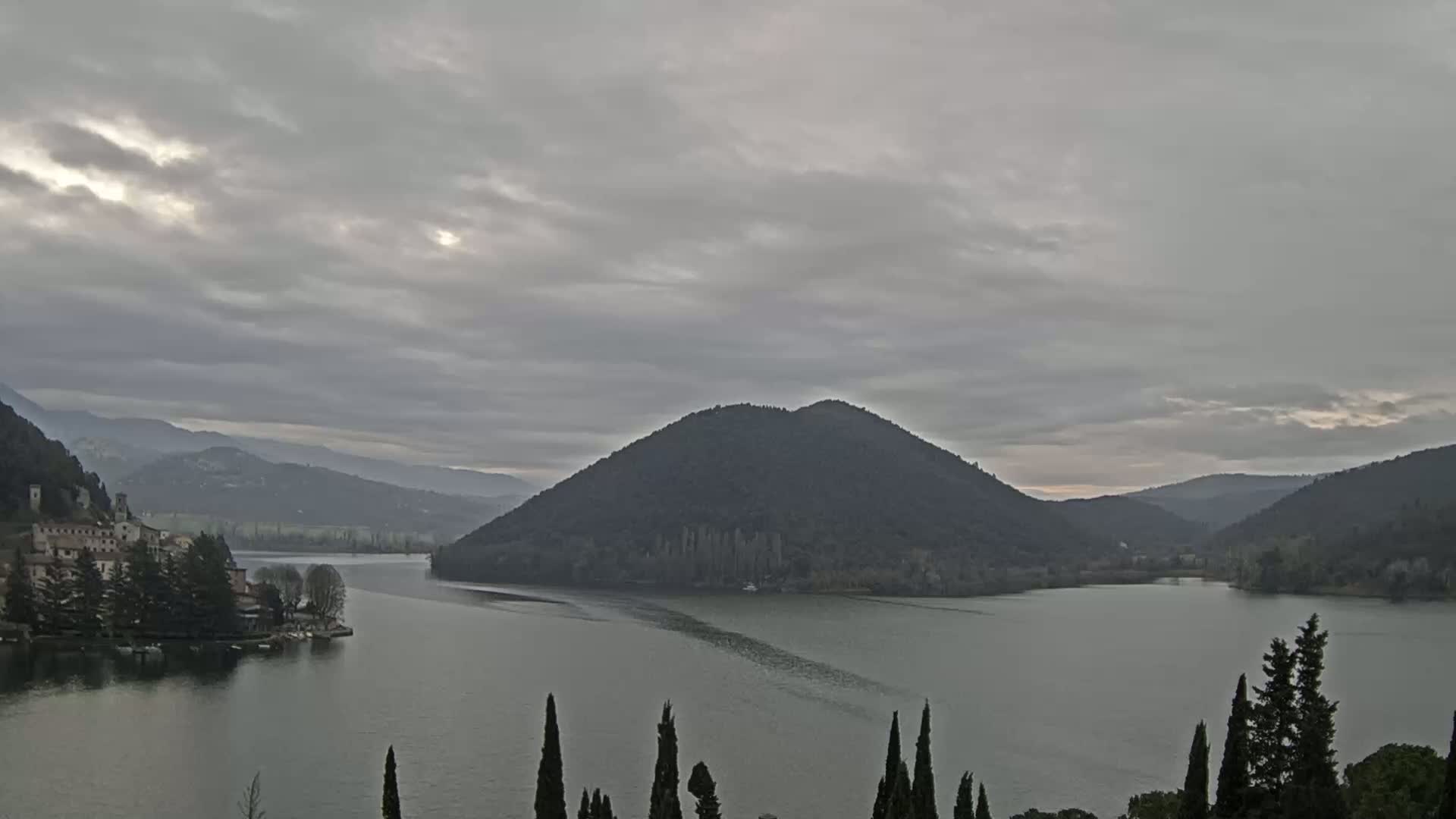 A lake is nestled between mountains under a cloudy sky, with a small village and island visible on one shore.