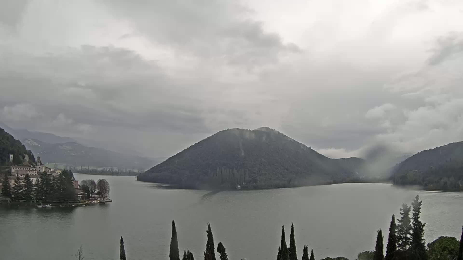 A lake is surrounded by mountains and a small town under an overcast sky.